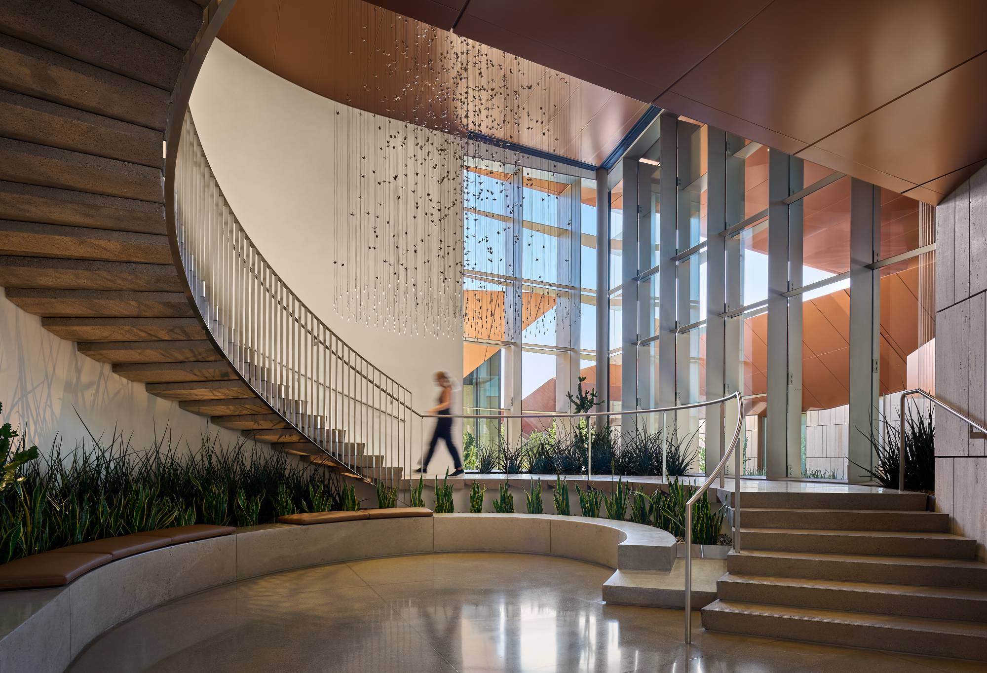 Person walking up winding staircase inside the Helios Education Campus' lobby.