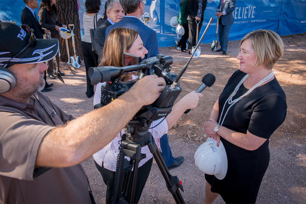 Jane LaRocca Roig being interviewed by reporters with cameras and microphones.